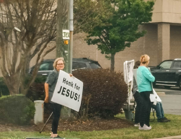 Frau hält ein Schild hoch "Honk for Jesus"