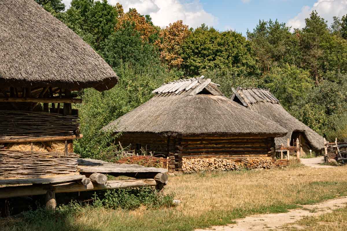 Drei strohgedeckte, niedrige Häuser im Grünen